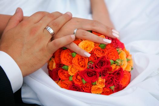 Close up portrait of newlywed man and wife holding hands over bouquet of colorful flowers and petals.