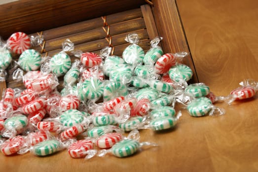 A closeup of peppermint swirl candies spilling from a wooden container.