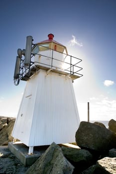 A small lighthouse on a rocky point against the sun