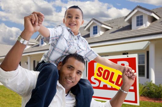 Excited Hispanic Father and Son with Sold For Sale Real Estate Sign in Front of House.