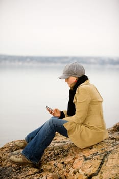 A young woman sitting by the ocean using a cell phone