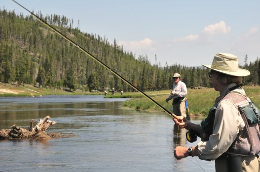 Active senior couple wading in the Firehole River (Yellowstone National Park) and fly-fishing for trout.