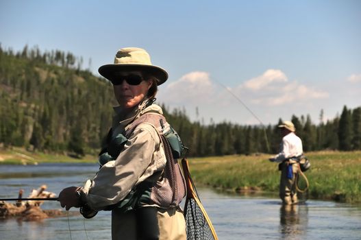 Active senior couple wading in the Firehole River (Yellowstone National Park) and fly-fishing for trout.