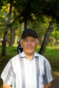 Portrait of the elderly man in a cap and a striped shirt against the nature