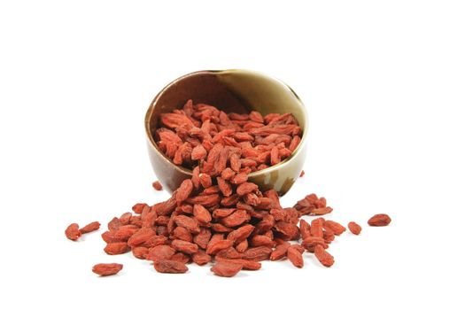 Red dry goji berries spilling out of a green and brown dish on a reflective white background
