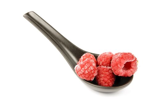 Red ripe frozen raspberries on a small black spoon with a reflective white background