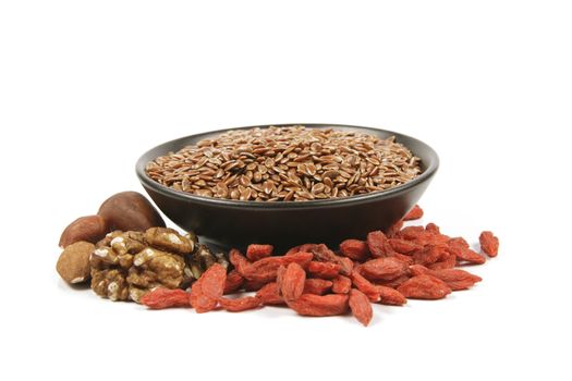 Brown linseed seeds in a small black bowl with mixed nuts and goji berries on a reflective white background