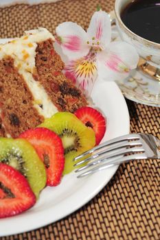 A slice of Carrot Cake, sliced strawberries and kiwi fruit with a cup of Coffee.