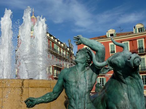 Sculpture of a man and a bull at the place Massena fountain in Nice, France, in front of red old buildings by beautiful weather