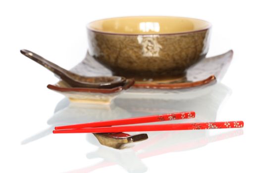 Pair of red chopsticks on white background with set of ceramic japanese dishware