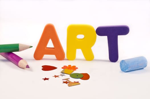 close and low level angle capturing coloured foam letters spelling the word 'ART' arranged over white and surrounded by art and craft materials.