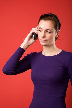 A casual portrait of a brunette caucasian female talking on a cell phone with a red background