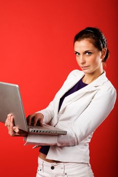 A young business woman or student using a laptop with a strong red background