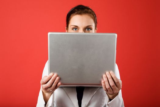 A young woman hiding behind and using a laptop computer wirelessly