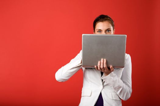 A young woman hiding behind and using a laptop computer wirelessly