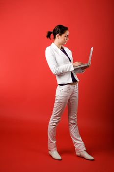 A young woman typing on a laptop computer isolated on red