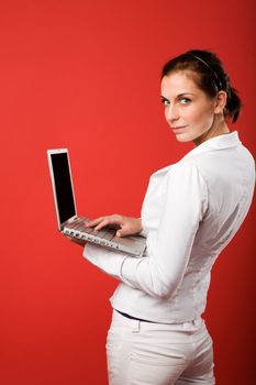 A young woman typing on a laptop computer isolated on red