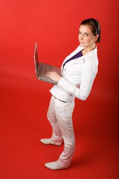 A young woman typing on a laptop computer isolated on red