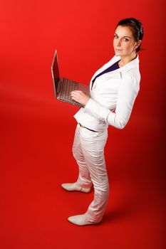 A young woman typing on a laptop computer isolated on red