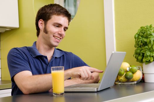 A young male using a laptop computer in the kicthen, smiling and laughing at what he sees