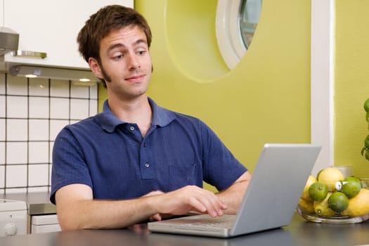 A young male using a laptop computer in the kicthen