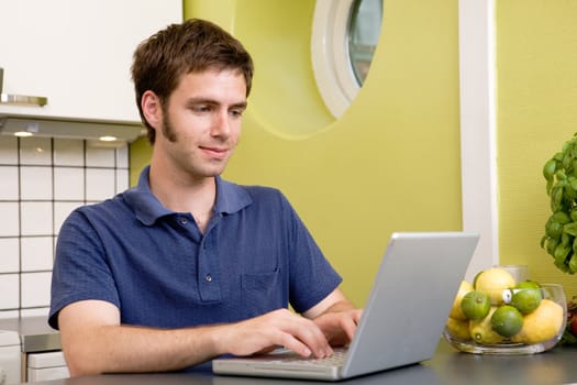 A young male using a laptop computer in the kicthen