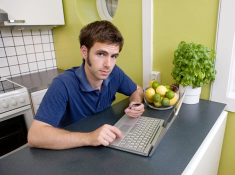 A young male shops online with a credit card at home in the kitchen.