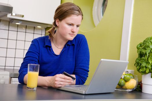 A young female making an online purchase from her kitchen.