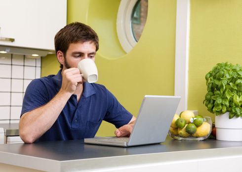 Using a laptop computer in the kitchen while enjoying a warm drink