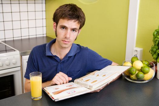 A young man in the kitchen looking at recipes.