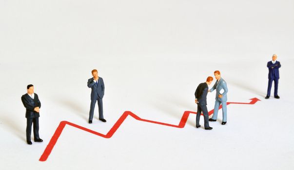 Group of managers (model railroad figures) positiones around graph showing rising business development.