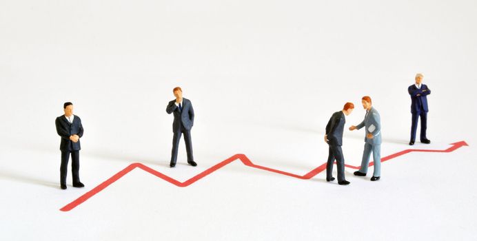 Group of managers (model railroad figures) positiones around graph showing rising development