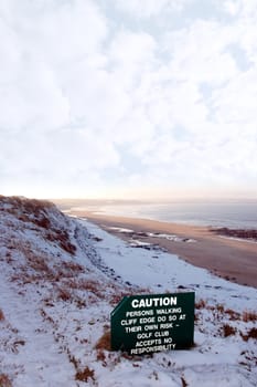 a caution sign on a cliff edge in snow covered ballybunion