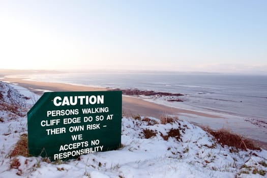 a caution sign on a cliff edge in snow covered ballybunion