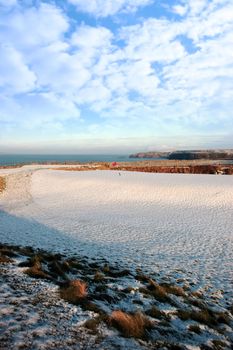 snow covering on a golf course in ireland in winter with sea and cliffs in background