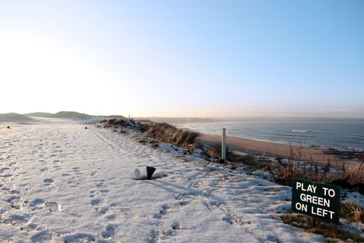 snow covering on a golf course in ireland in winter with green play sign