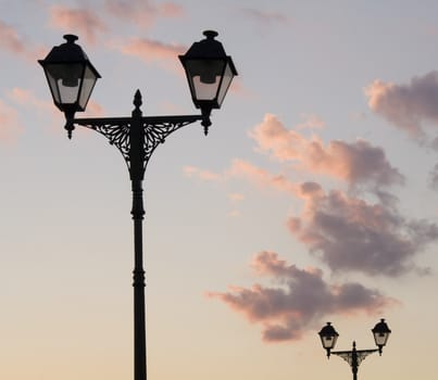 Two street lamp silhouettes on sky background in sunset time