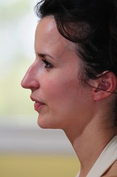 Profile view of a beautiful young woman with dark hair in a white halter top, in front of a window.