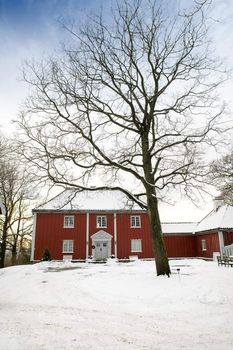 A large red wooden house in a nice neighborhood surrounded by bushes.