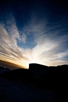 A rock landscape near the ocean during a sunset and a dramatic sky.