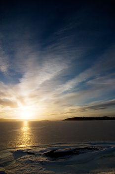 A golden sunset going down behind a hill over a frozen lake - fjord.  Oslo fjord in March.