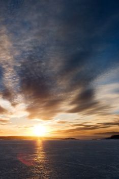 A golden sunset going down behind a hill over a frozen lake - fjord.  Oslo fjord in March.