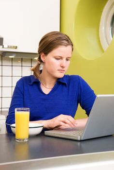 A young woman using the computer at breakfast or eating a meal in the kichen.