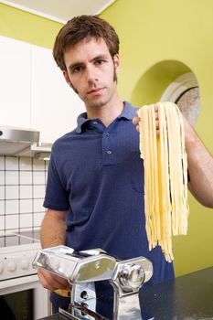 A proud young man with fresh homemade fettuccine looks at the camera- shallow depth of field with focus on the pasta