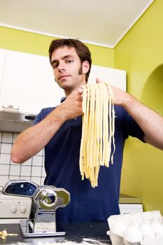 A proud young man with fresh homemade fettuccine looks at the camera- shallow depth of field with focus on the pasta