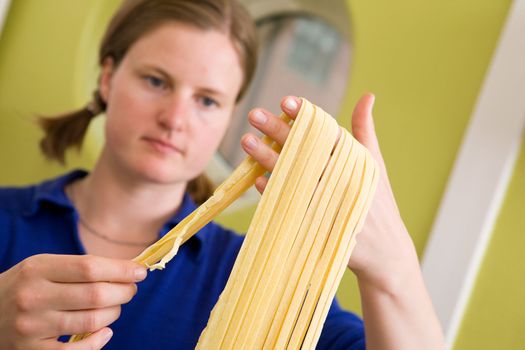 A proud young woman with fresh homemade fettuccine - shallow depth of field with focus on the pasta