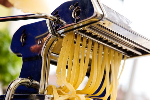 Fettuccine coming out of a manual pastamachine - shallow depth of field with focus on the pasta