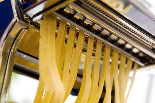 Fettuccine coming out of a manual pastamachine - shallow depth of field with focus on the pasta