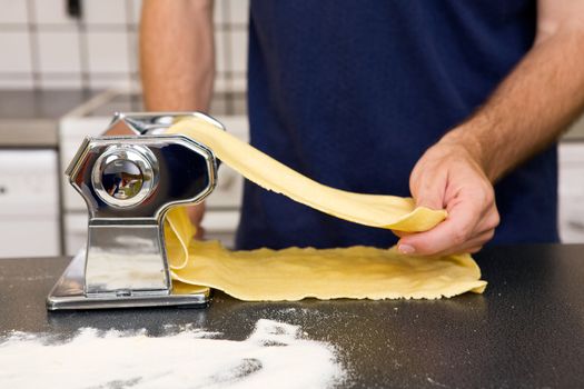 A Male making pasta on the counter in the kitchen.