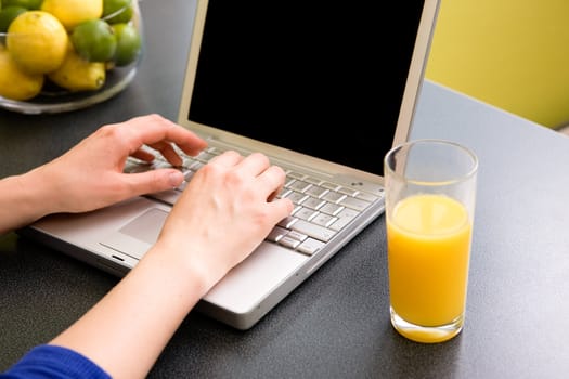 A computer in the kitchen with a female hand using the touch pad.  The laptop has a completely black screen for easy editing.